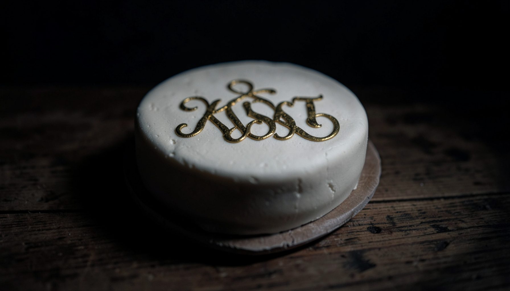 Kue monogram dengan huruf dekoratif di atas meja kayu, warna netral dengan aksen keemasan, suasana artisan